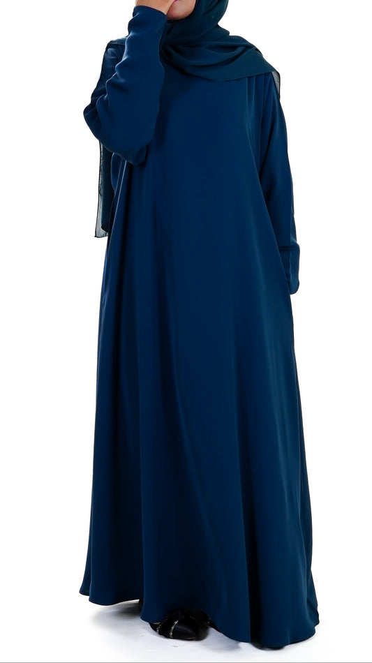 Woman wearing a long deep teal abaya with a matching hijab on a white background