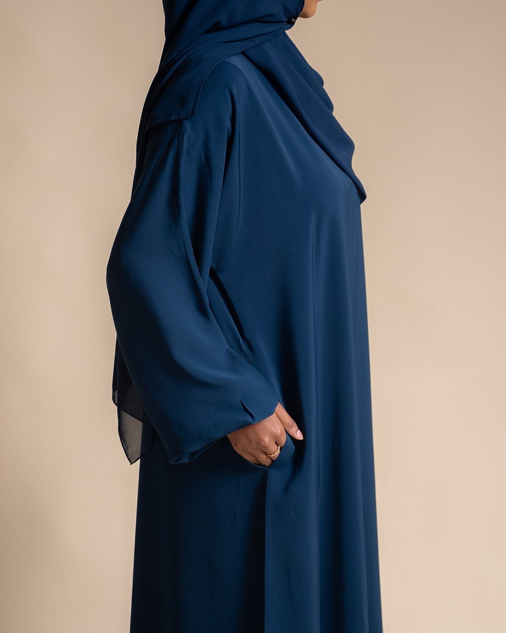 Navy blue abaya worn by a person on a beige background
