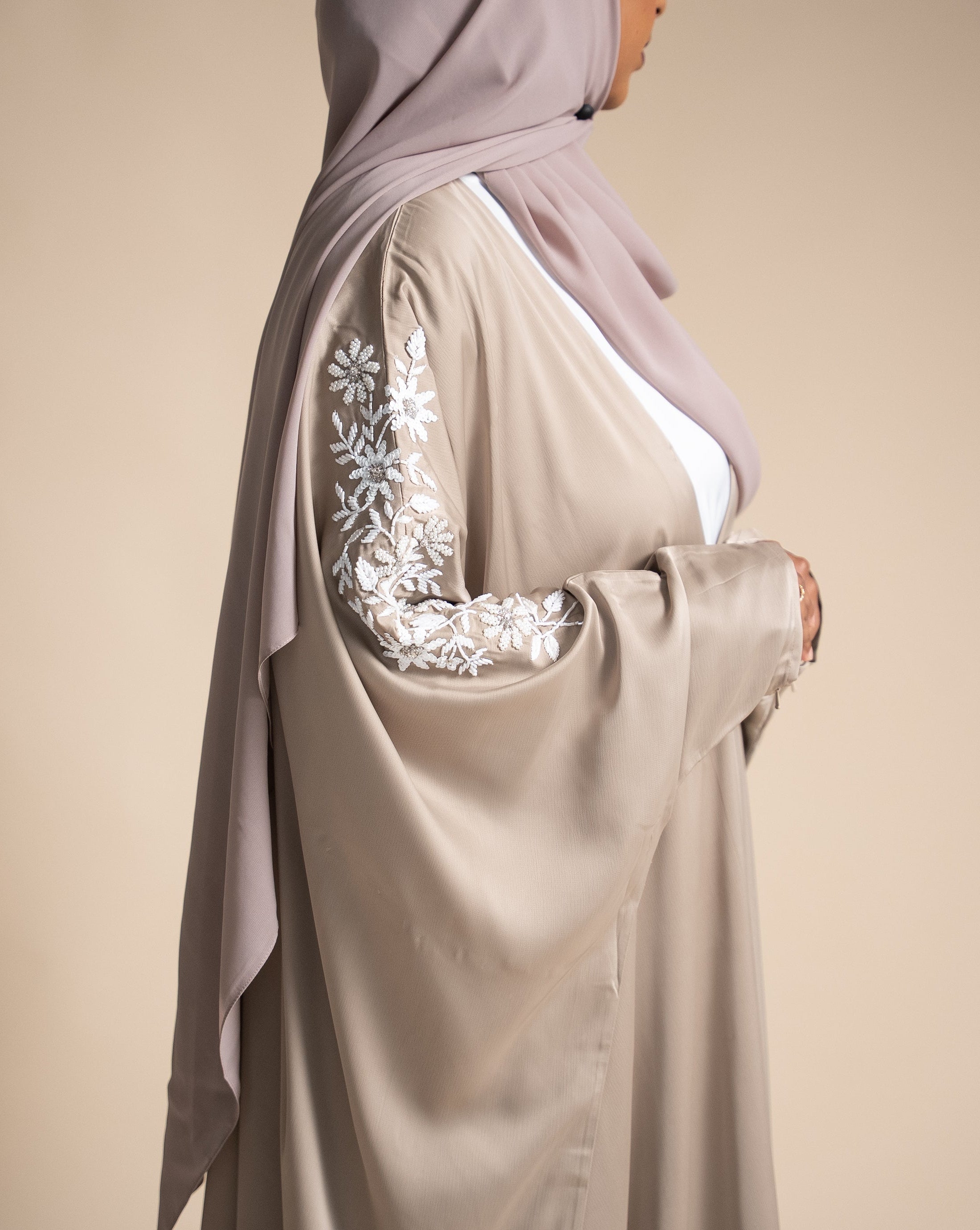 Beige abaya with floral embroidery on sleeves against a beige background