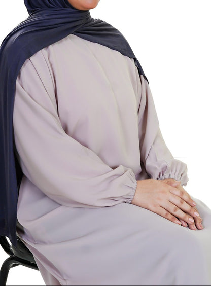Woman wearing a light gray abaya with a dark blue hijab on a white background