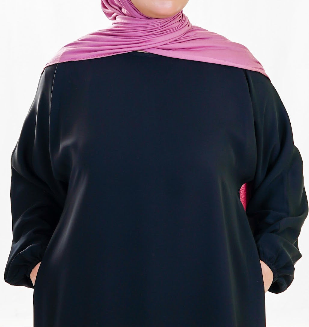 Person wearing a black abaya with a pink hijab on a white background