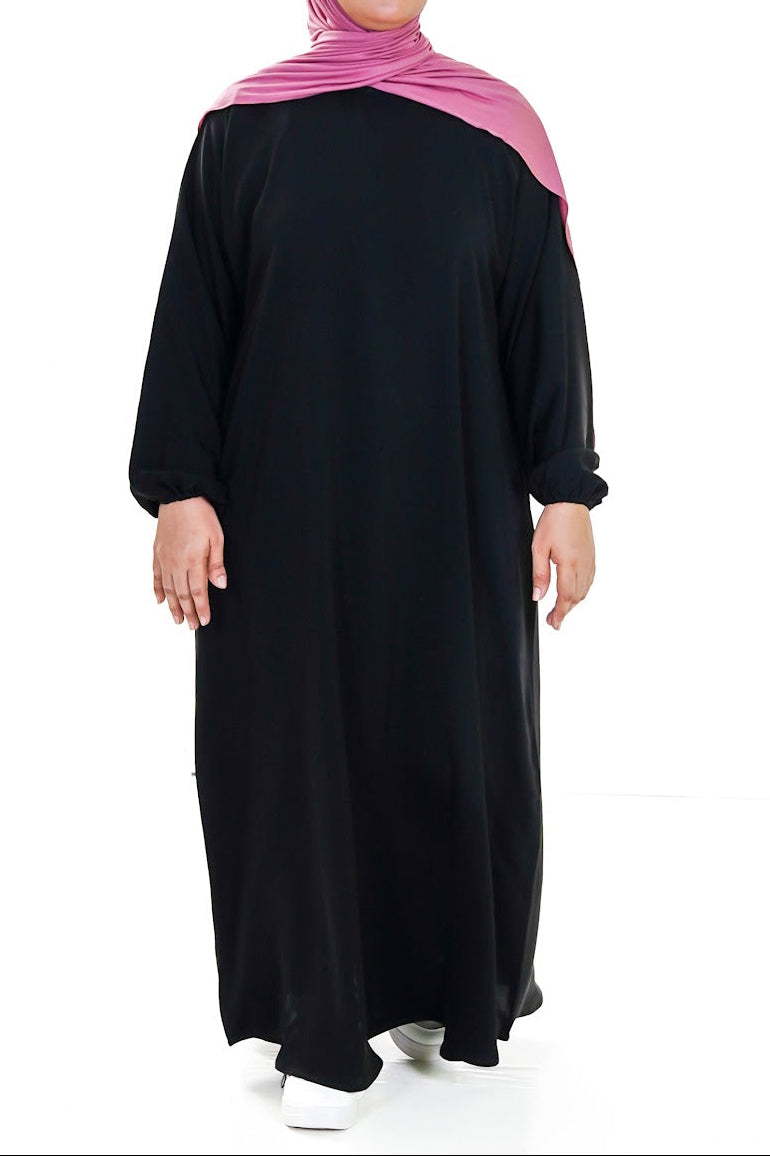 Person wearing a black affordable abaya with a pink hijab on a white background