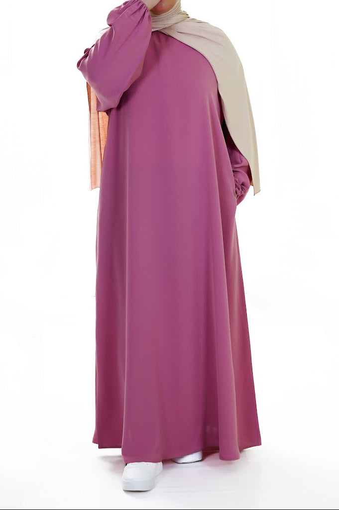 Woman wearing a long pink abaya with a matching hijab on a white background