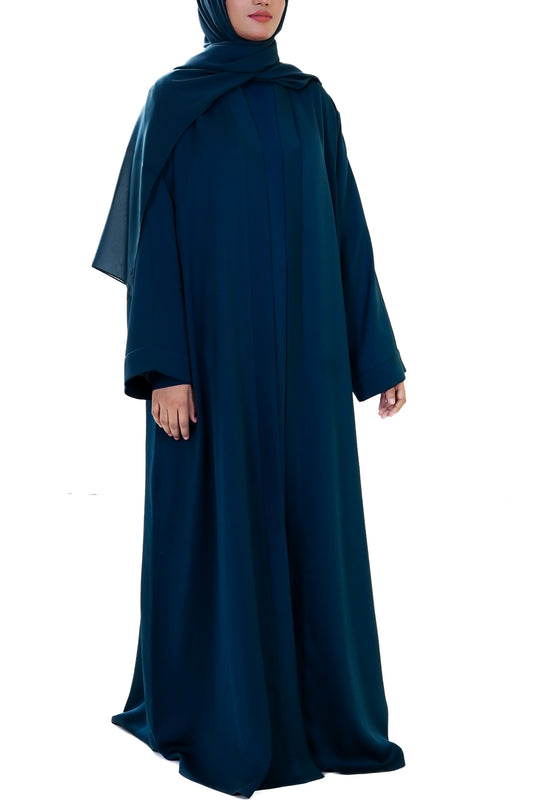 Woman wearing a long deep teal abaya with a matching hijab on a white background