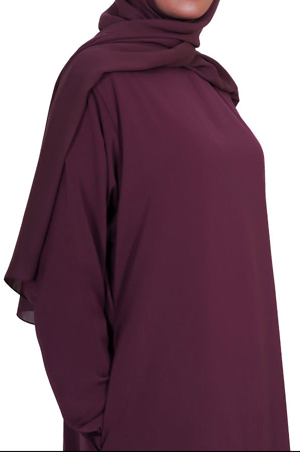 Woman wearing a dark purple hijab and dress on a white background
