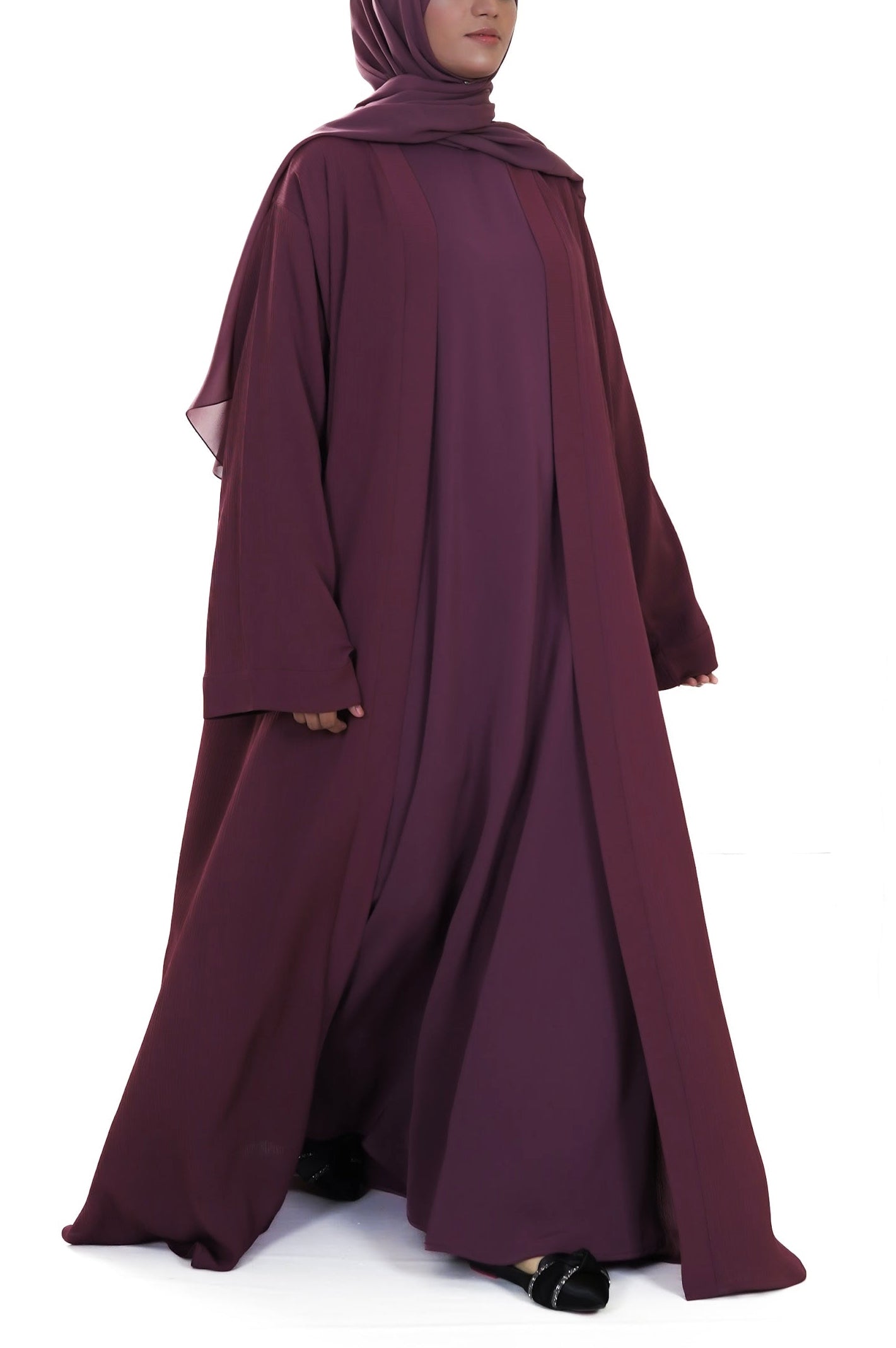 Woman wearing a long burgundy abaya with a matching hijab on a white background