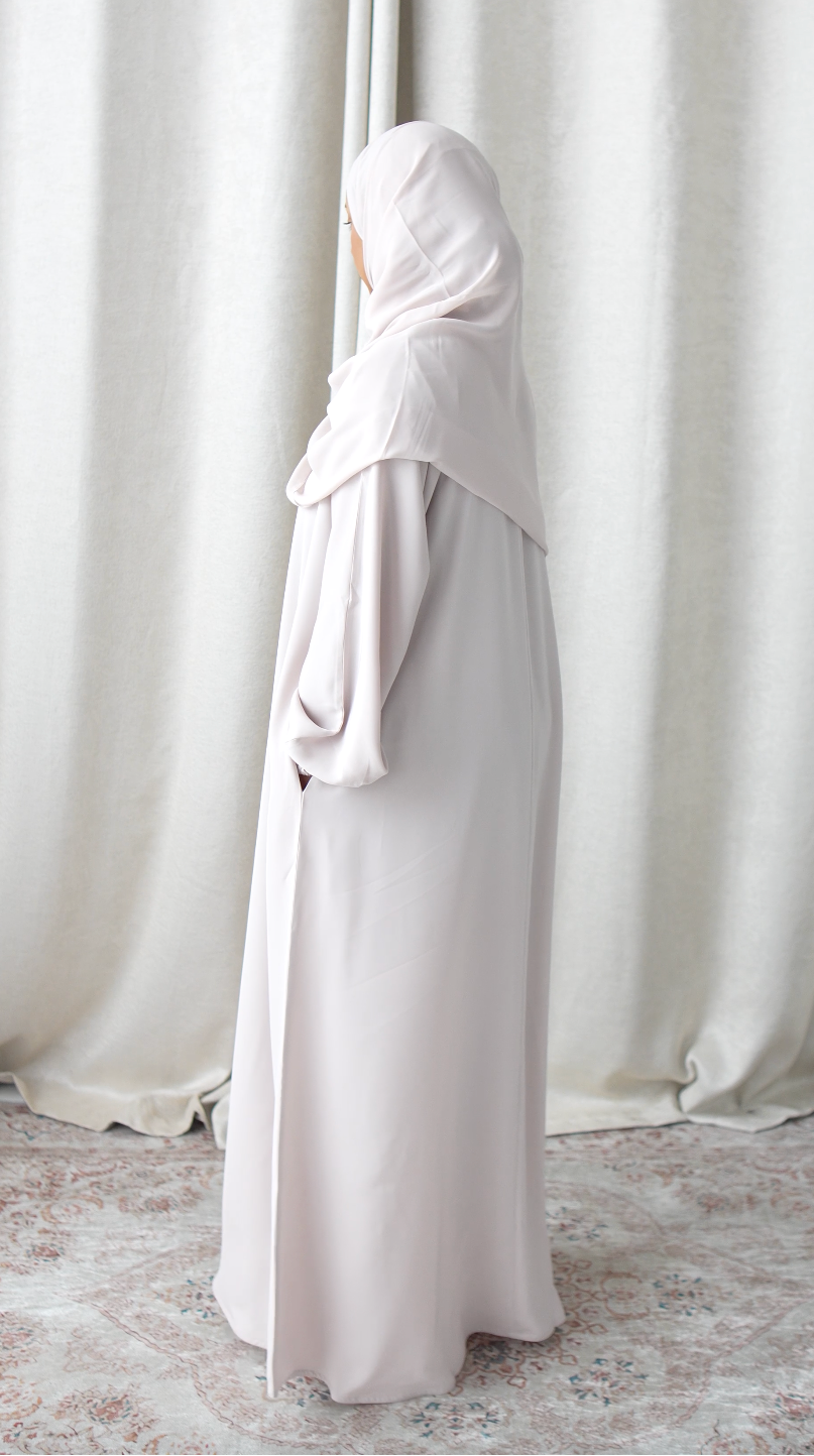 Person wearing a long, light-colored dress standing in front of white curtains.